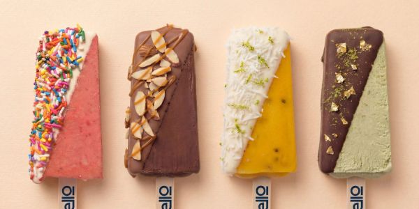 Four colorful popsicles with various toppings on a beige background.