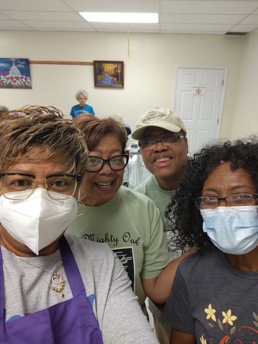 A group of four women, two wearing masks, smiling indoors.