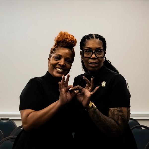 Two women posing, wearing black, making hand gestures.