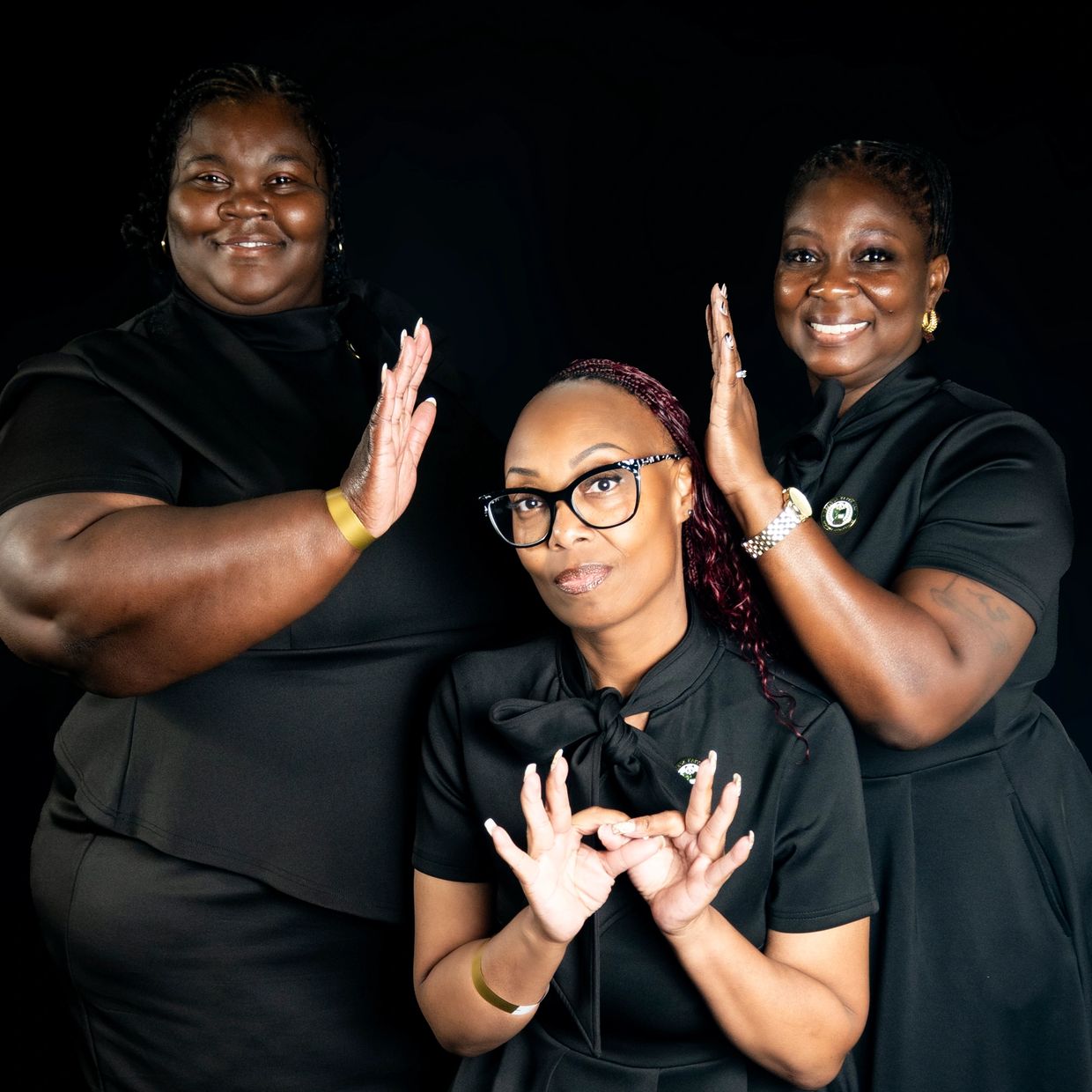 Three women posing with hand signs against a black background.