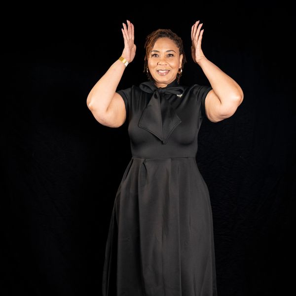 Smiling woman in a black dress with raised hands.