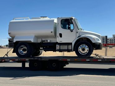 A white truck is on the back of a flatbed trailer.