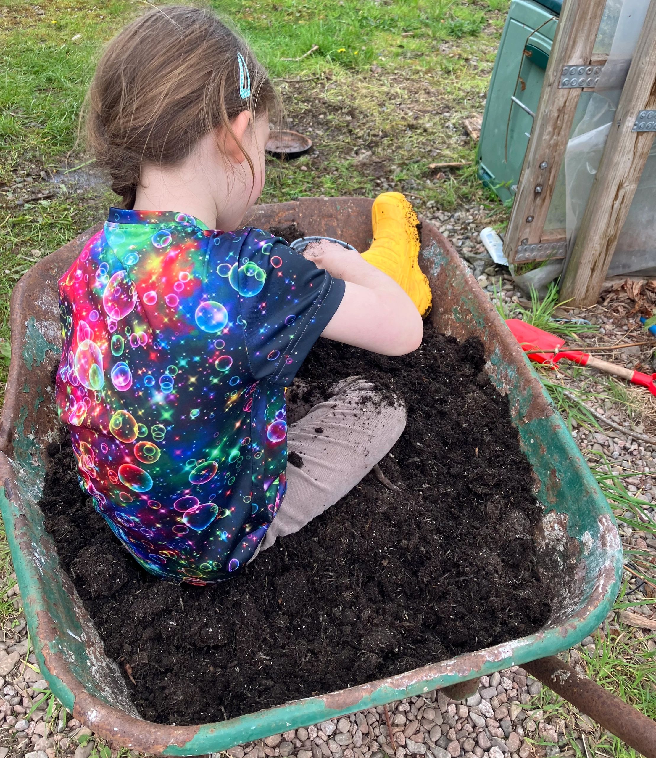 Child sitting in wheelbarrow in soil sensory play