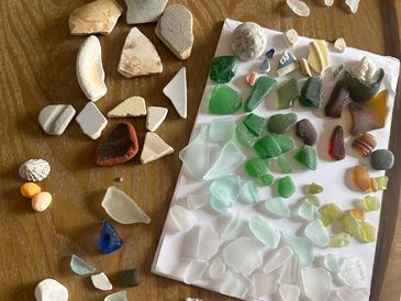Various sea glass and ceramic pieces sorted by color on a wooden table.