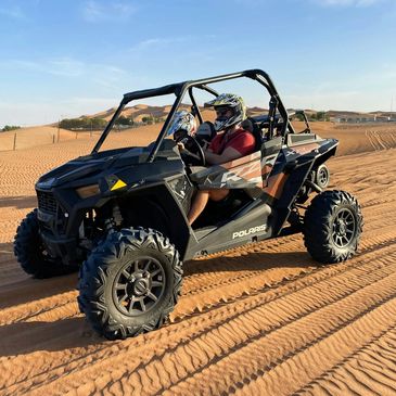 Two people driving a Polaris RZR off-road vehicle in the desert.