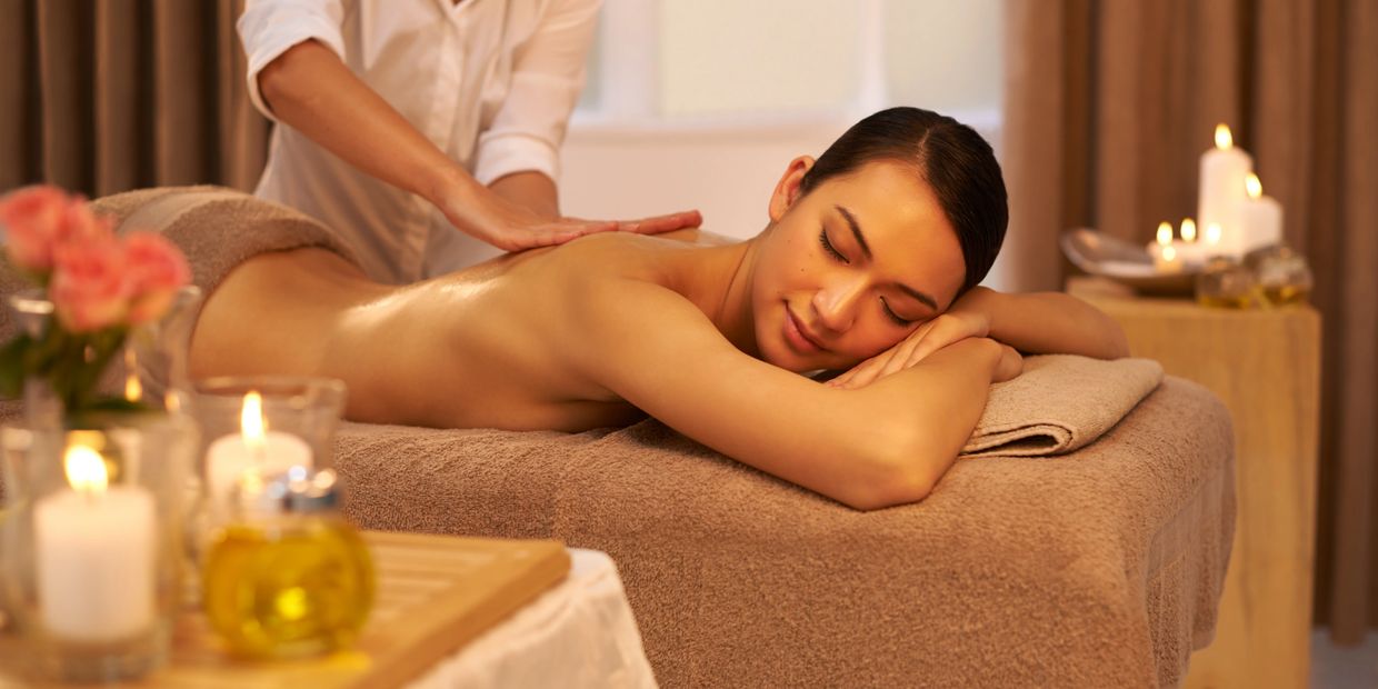 A woman on a massage table enjoys a massage while candles are lit on each side.