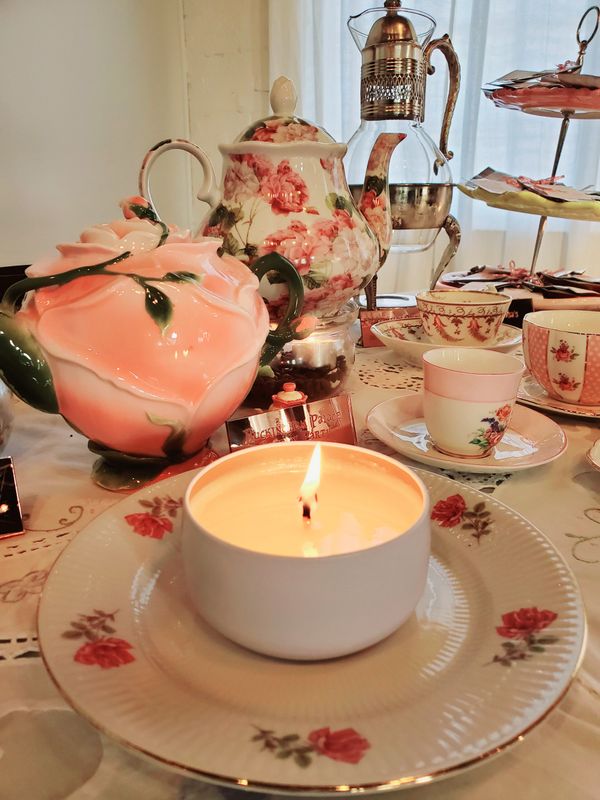 small candle sitting on a tea cup sauce with beautiful tea pots and cups surrounding it. 