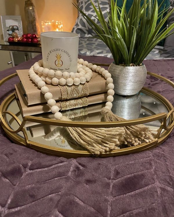 Candle with greenery and a strand of wooden beads on a glass tray.