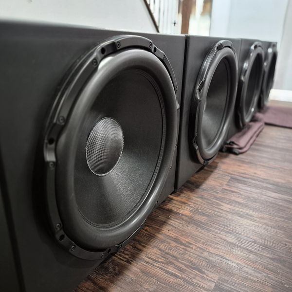 Close-up of four large black speakers on a wooden floor.