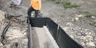 Person standing next to a trench lined with concrete and black mesh.
