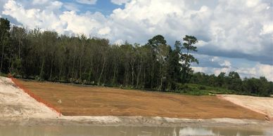 A cleared land area bordered by trees and a cloudy sky.