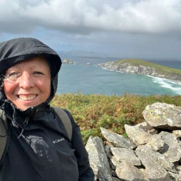 Smiling woman in outdoor gear by rocky coastline.