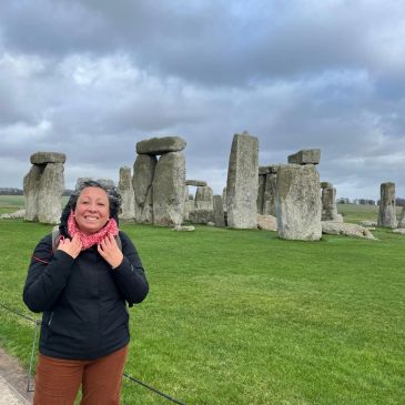 Woman smiling at Stonehenge under cloudy sky.