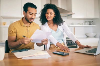 Couple reviewing documents together at a kitchen table with a laptop.