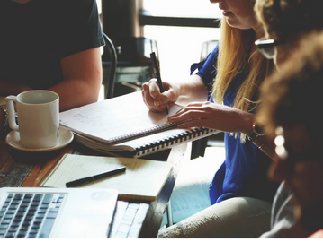 People collaborating with notes, laptop, and coffee in a casual meeting.