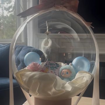 Transparent balloon with a pink bow holding a plush toy and decorations.