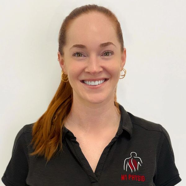 Smiling woman with red hair in a black M1 Physio shirt.