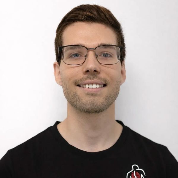 Smiling young man wearing glasses and a black t-shirt with a logo.