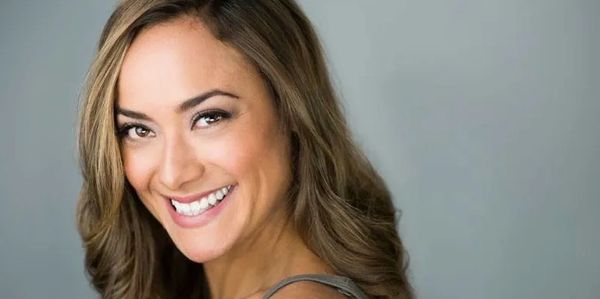 Smiling woman with wavy light brown hair poses against a gray background.