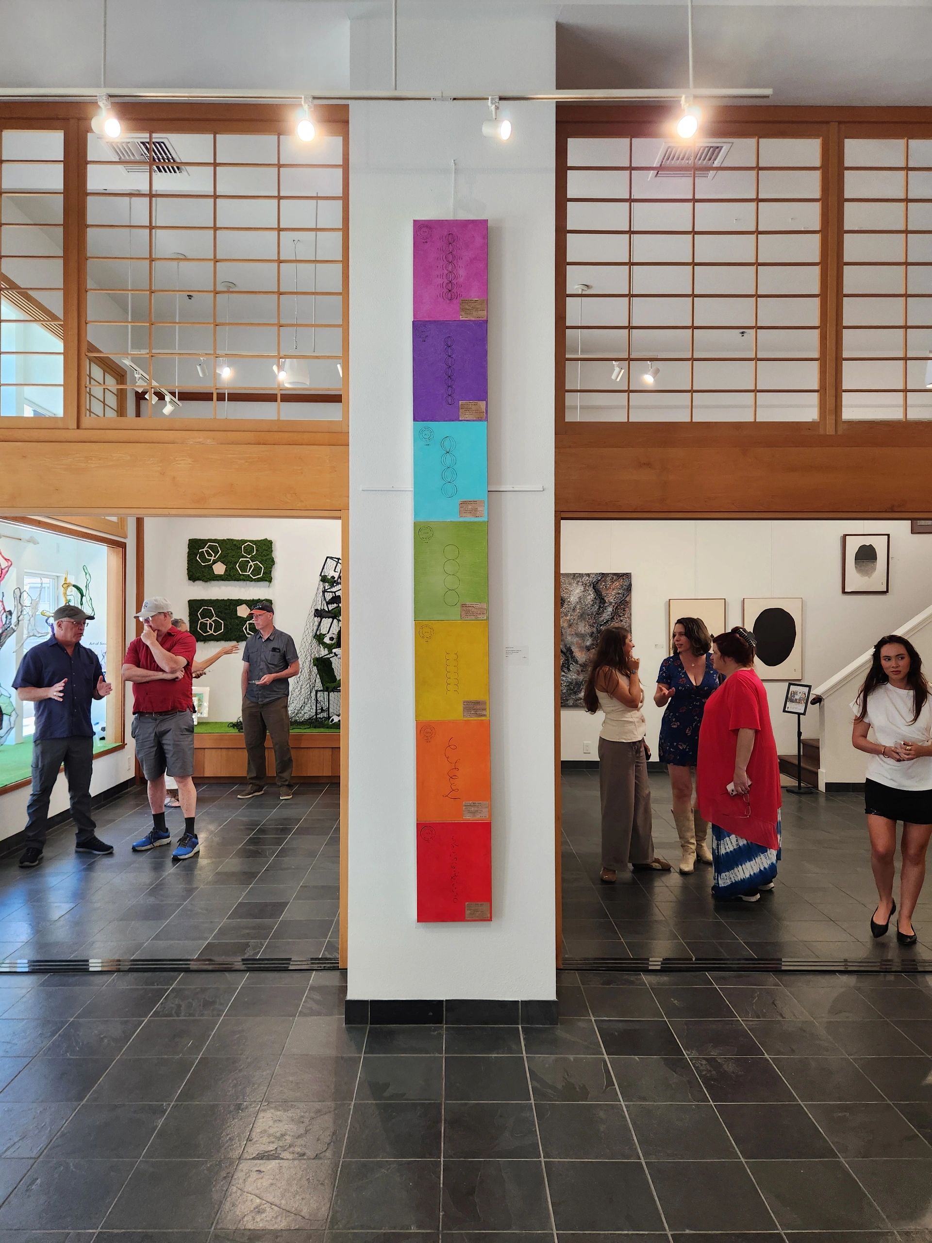 Colorful vertical artwork displayed in a gallery with visitors.