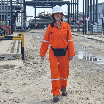Woman in orange safety suit and helmet walking in industrial area.