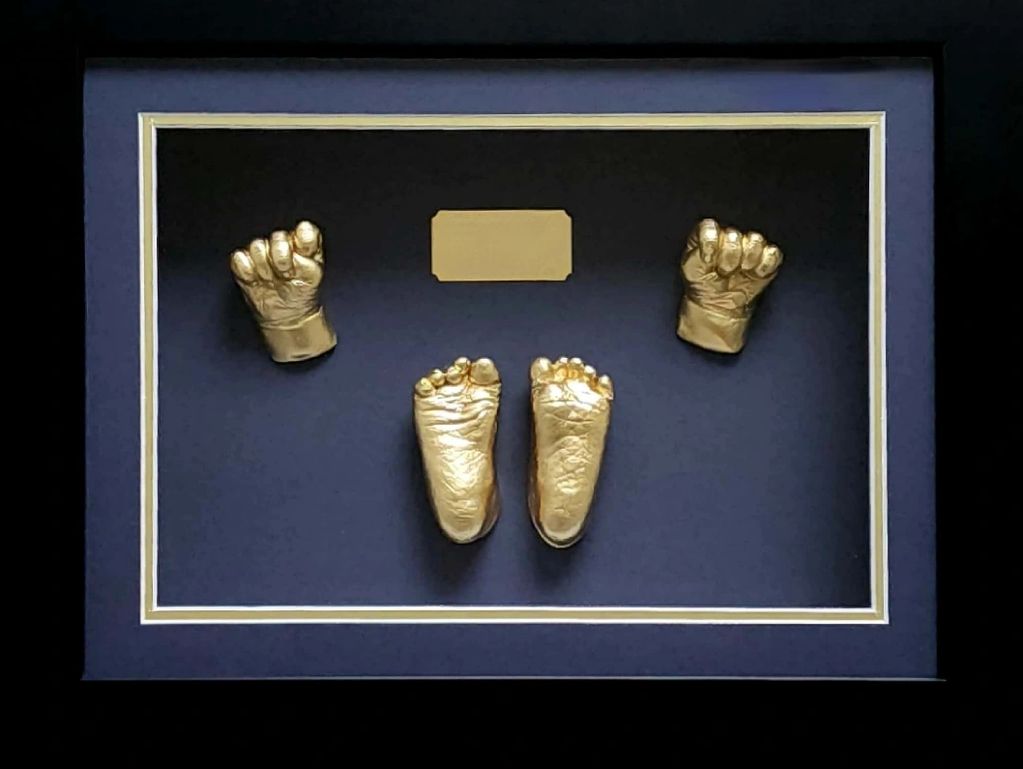 Golden baby hand and foot casts framed on a dark background.