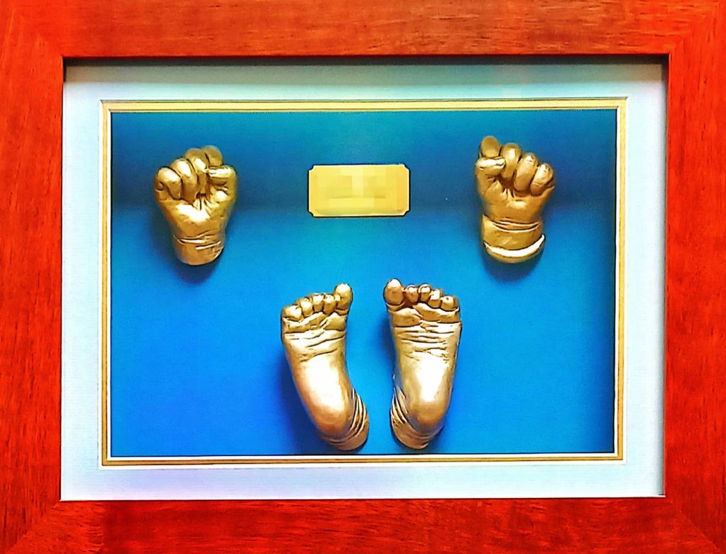 Golden baby hand and foot casts in a wooden frame with a blue background.
