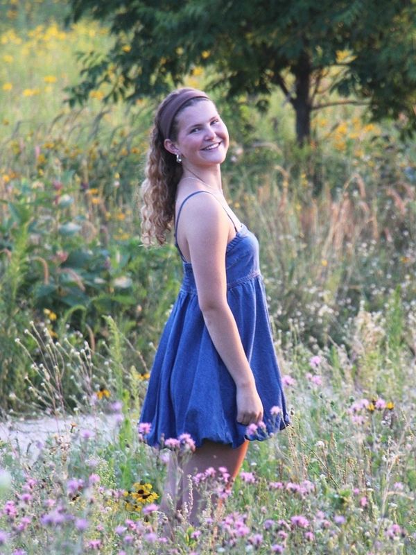 Young woman in a blue dress smiling in a wildflower field.