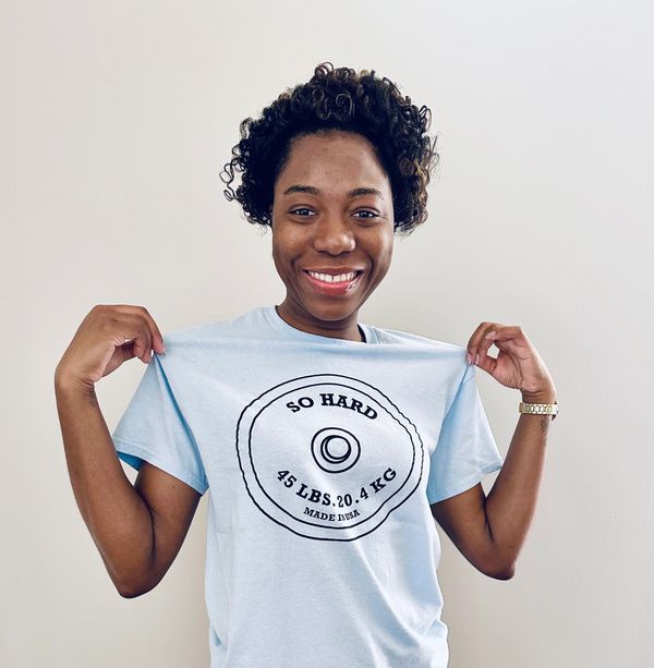 Smiling woman showing off a light blue weightlifting-themed t-shirt.