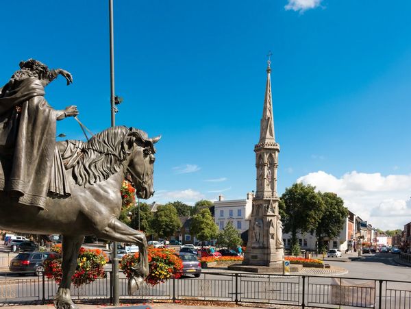 Statue of a man on a horse near a tall monument in a sunny town square.