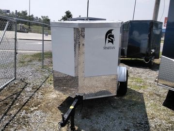 A small Spartan-branded enclosed trailer parked outdoors on gravel ground.