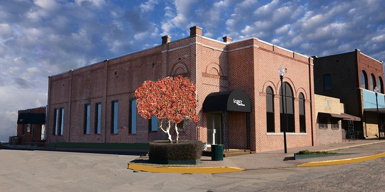 Brick building on a street corner with colorful tree and cloudy sky.