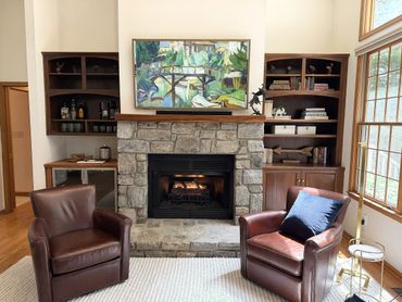 Stone fireplace living room at Woodsong Lake Toxaway Retreat with warm seating, wooded views, and comfortable interiors for seasonal mountain stays.