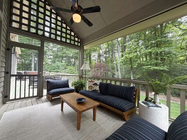 Screened porch at Woodsong Lake Toxaway Retreat with wooded views, comfortable seating, ceiling fan, and quiet mountain setting for seasonal stays.