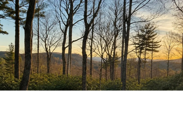 Sunset mountain view from Woodsong at Lake Toxaway with tree-framed Blue Ridge scenery and warm evening light from the deck area.