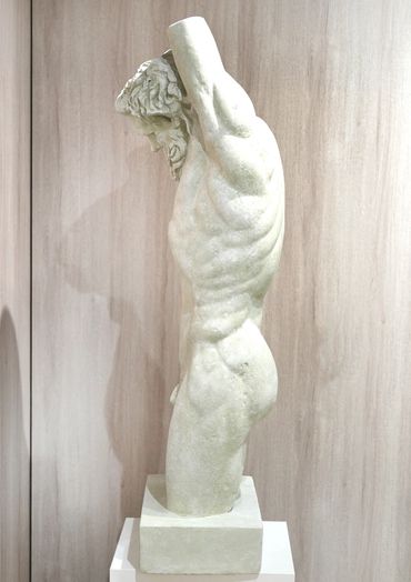 Side view of a classical marble statue of a muscular male figure with arms raised.