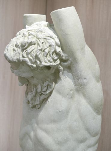 Close-up of a headless, armless ancient marble statue showing detailed hair and muscular torso.