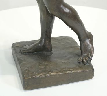 Close-up of the modeled legs and feet of Athlete, Male Nude, showing the bronze-toned plaster surfac