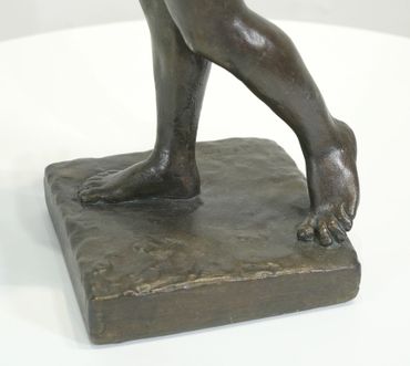 Close-up of bronze sculpture showing feet and lower legs on a textured base.