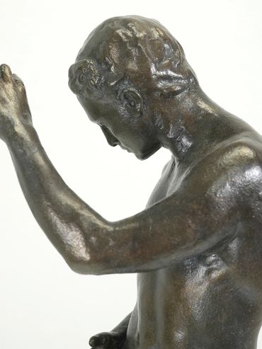 Bronze statue of a man with raised arm and bowed head.