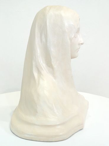Side view of a white marble bust of a veiled woman on a white table.