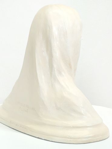 A smooth white sculpture resembling a draped cloth or covered object on a round base.