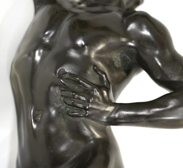 Close-up of a bronze sculpture showing a hand gripping a torso.