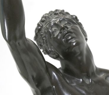 Close-up of a dark bronze statue showing a man with an expressive face and raised arm.