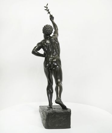 Bronze statue of a nude male figure holding a branch, viewed from behind.