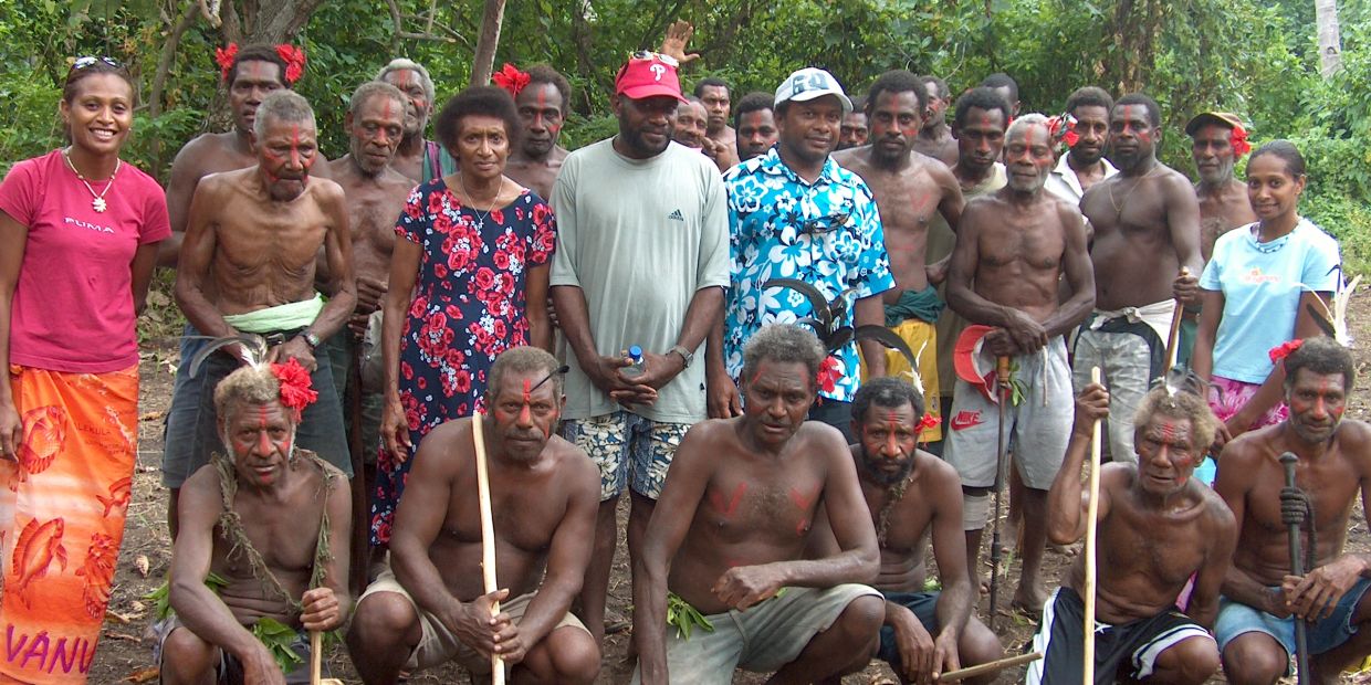 A diverse group of indigenous people posing outdoors with traditional attire and face paint.