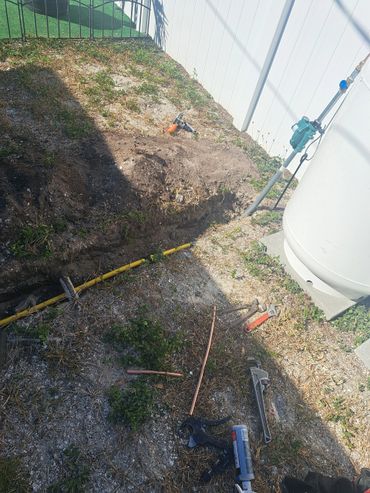 Tools and piping laid out near a dug trench next to a white fence.