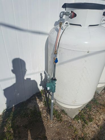 Large white propane tank with attached pipes and a pump outdoors.
