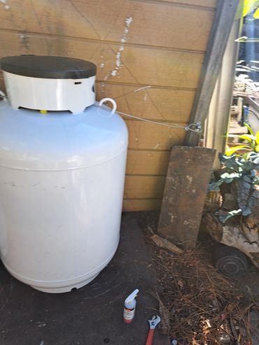 Large propane tank with tools on the ground near a wooden wall.