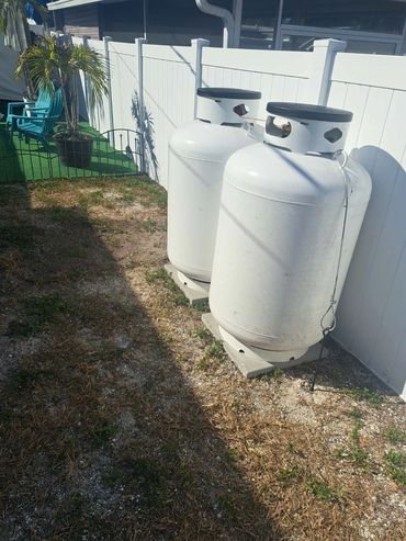 Two large white propane tanks secured by a fence in a backyard.
